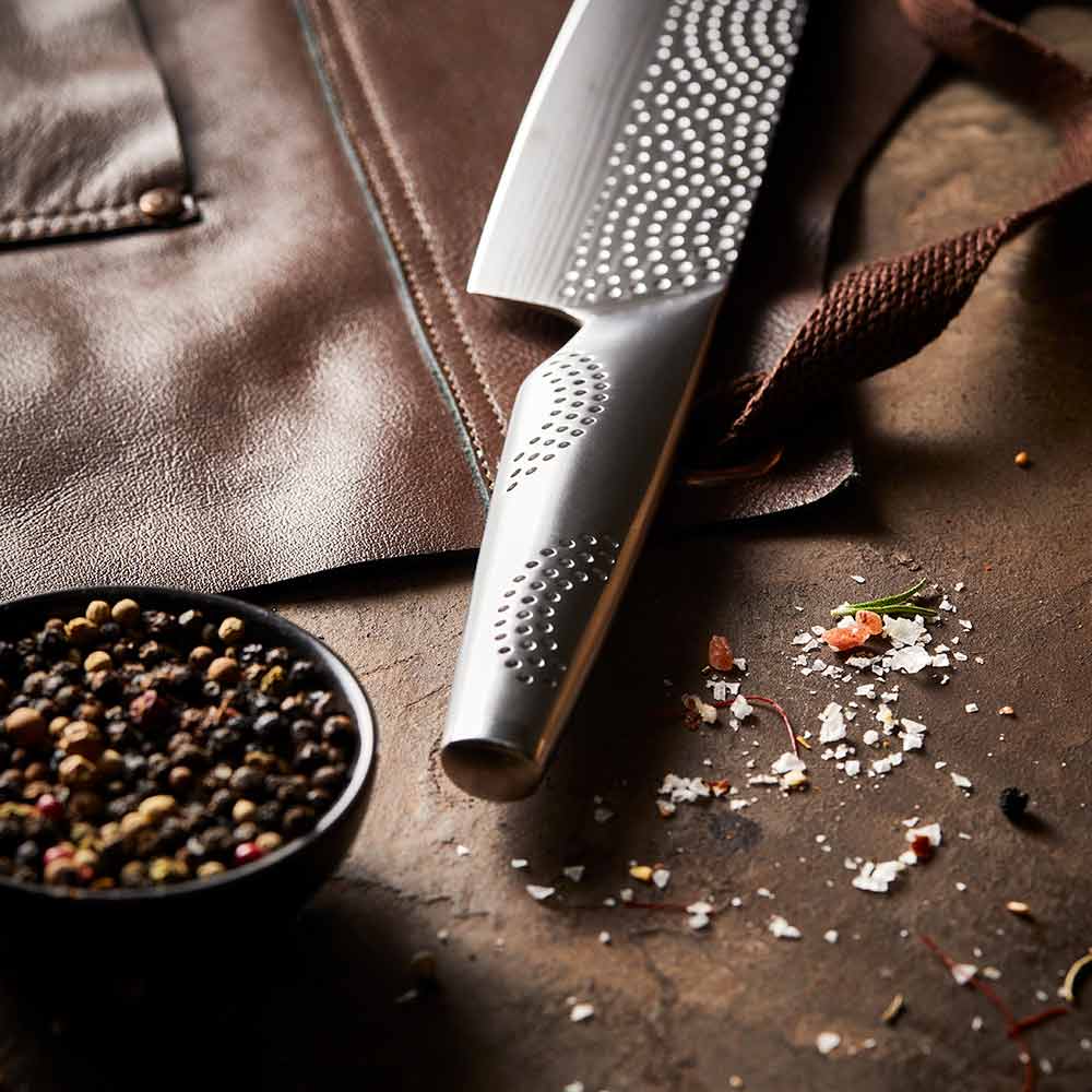 A person chops herbs in a kitchen with large steak in background on a wooden board - Baccarat