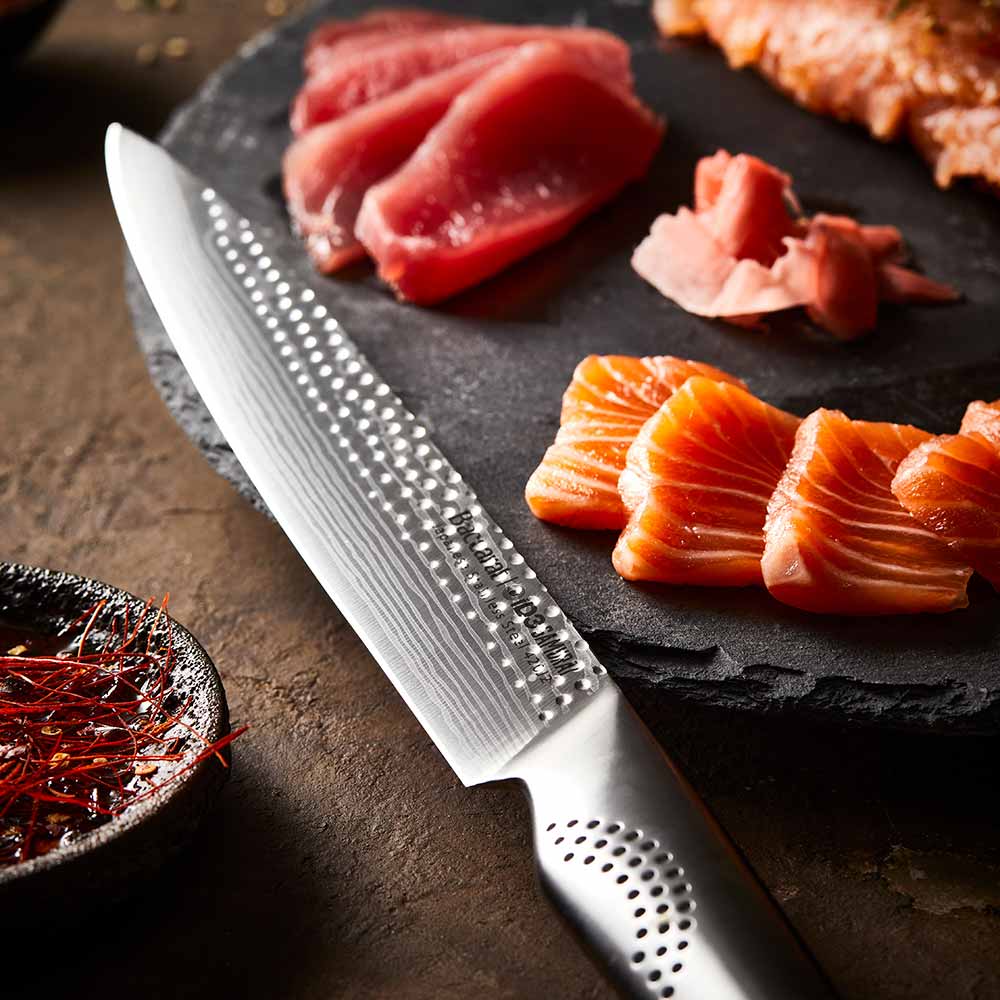 A sharp knife rests beside sliced raw fish on a slate board silver kitchen knife 20cm - Baccarat
