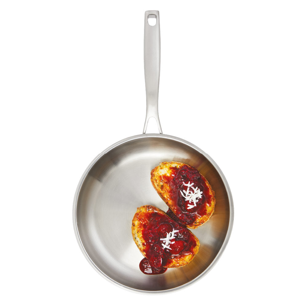 Person flips chicken with a black spatula in a stainless steel frying pan on wooden board - Baccarat