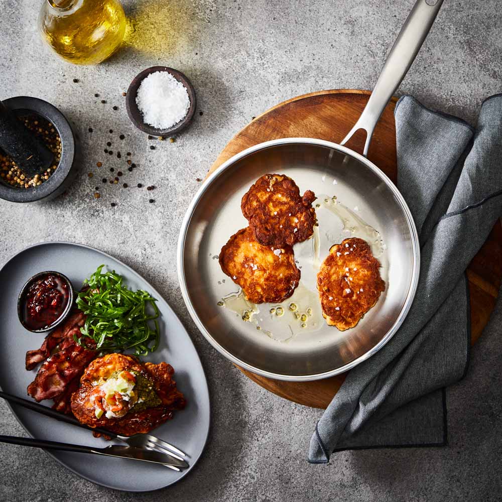Person flips chicken with a black spatula in a stainless steel frying pan on wooden board - Baccarat