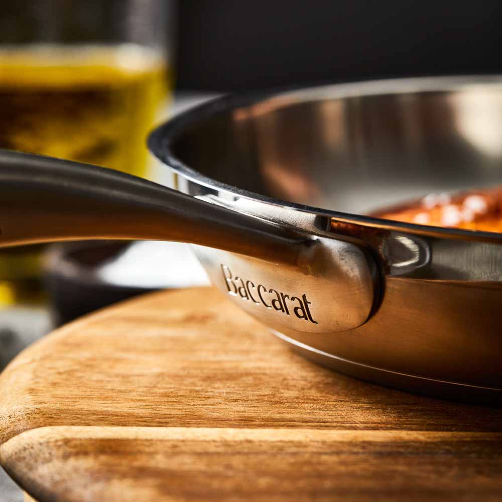 Person flips chicken with a black spatula in a stainless steel frying pan on wooden board - Baccarat