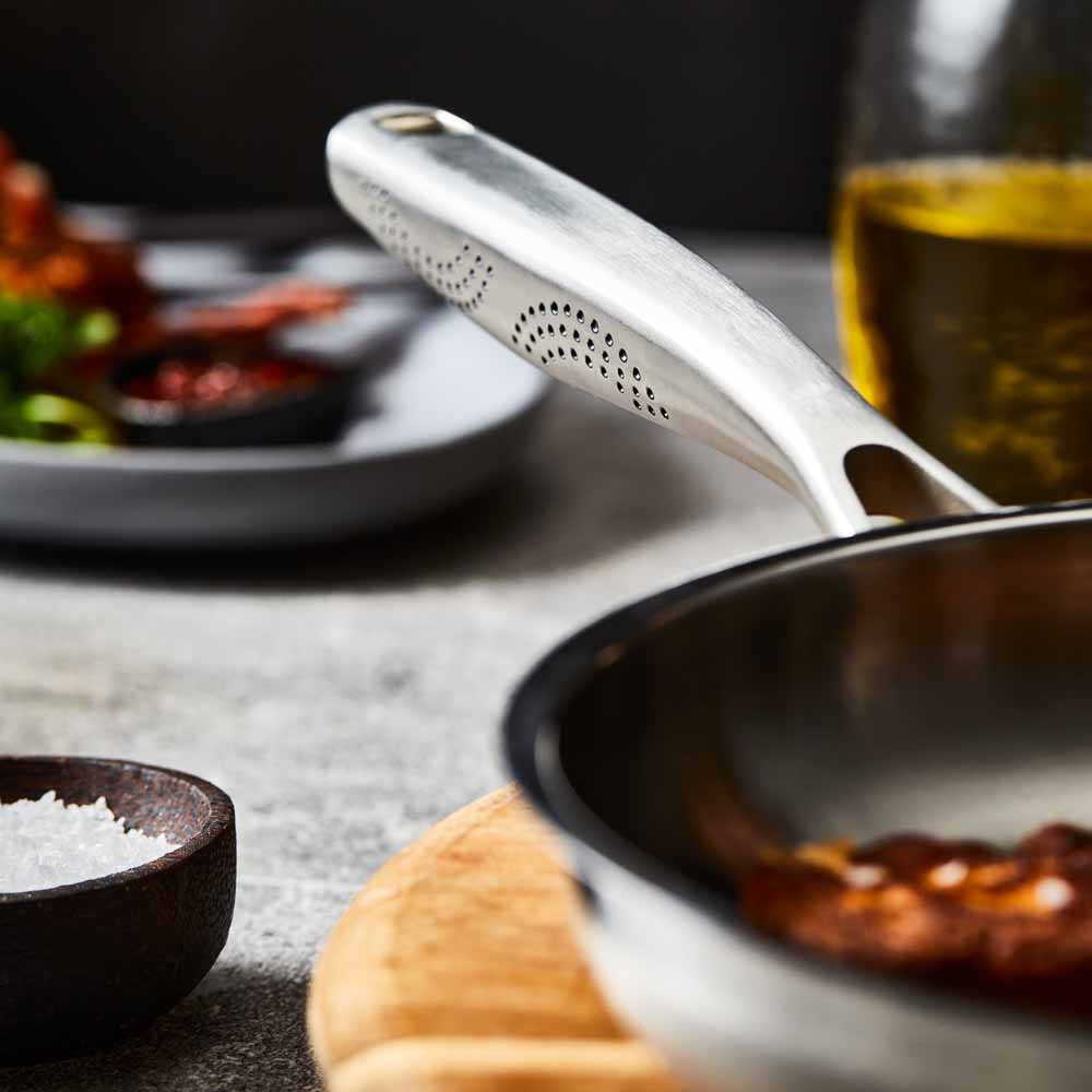 Person flips chicken with a black spatula in a stainless steel frying pan on wooden board - Baccarat