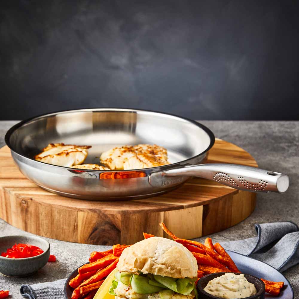 A stainless steel frying pan with a textured handle sits on a wooden board - frypan 26cm - Baccarat