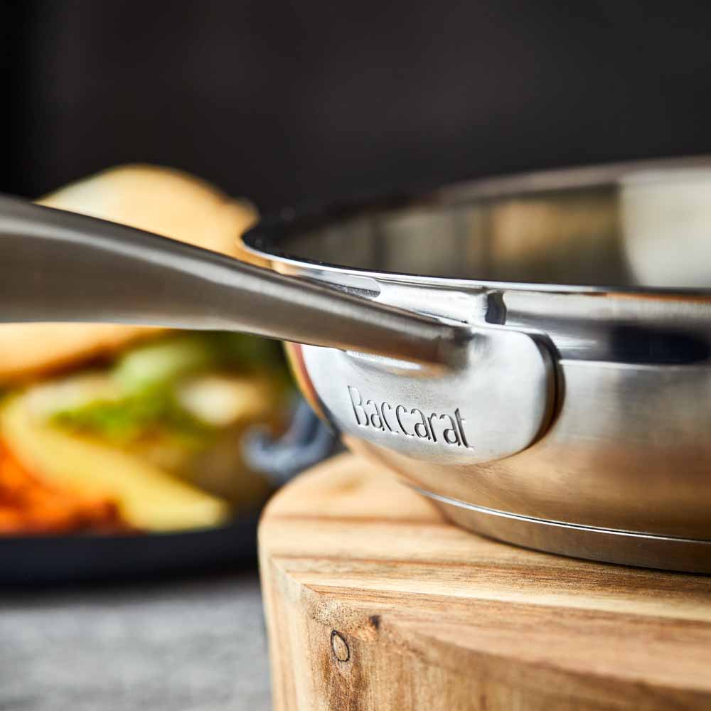 A stainless steel frying pan with a textured handle sits on a wooden board - frypan 26cm - Baccarat