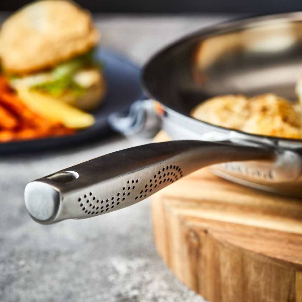 A stainless steel frying pan with a textured handle sits on a wooden board - frypan 26cm - Baccarat