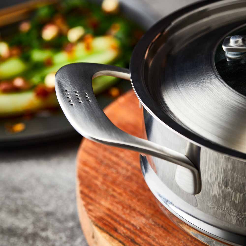 Hand lifting lid off stainless steel steamer with green vegetables on wooden board 32cm - Baccarat
