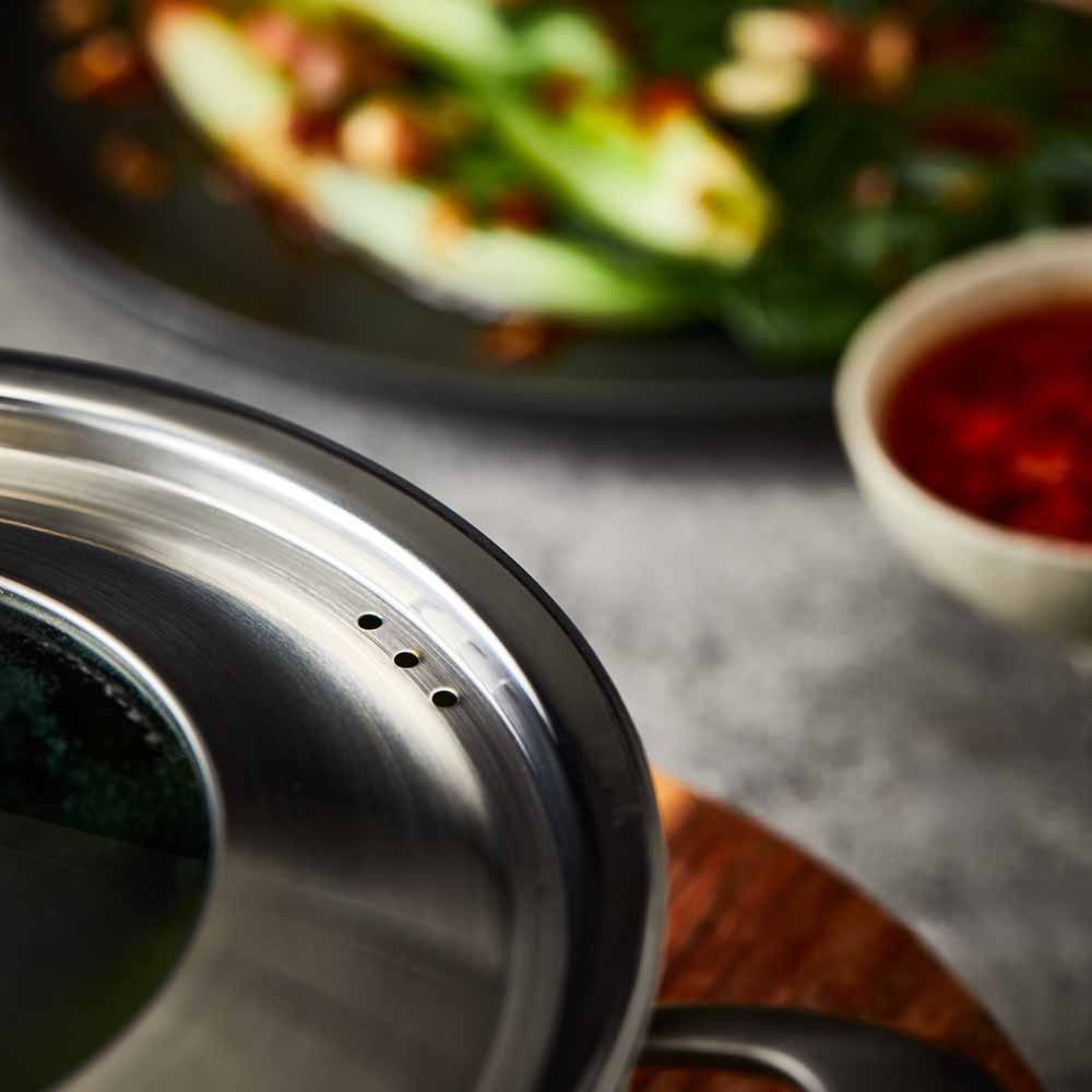 Hand lifting lid off stainless steel steamer with green vegetables on wooden board 32cm - Baccarat