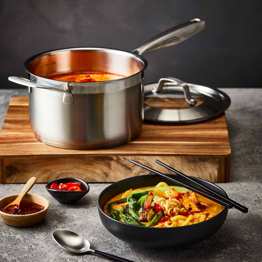 stainless steel saucepan 20cm pot of soup on a wooden board beside black bowl of noodles - Baccarat