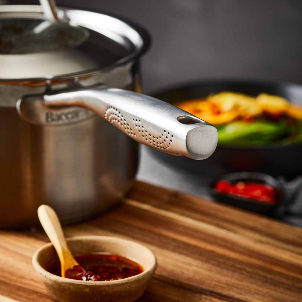 stainless steel saucepan 20cm pot of soup on a wooden board beside black bowl of noodles - Baccarat