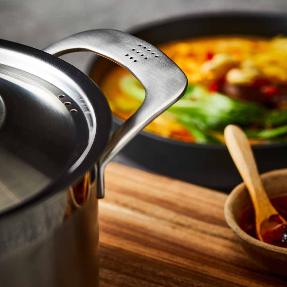 stainless steel saucepan 20cm pot of soup on a wooden board beside black bowl of noodles - Baccarat