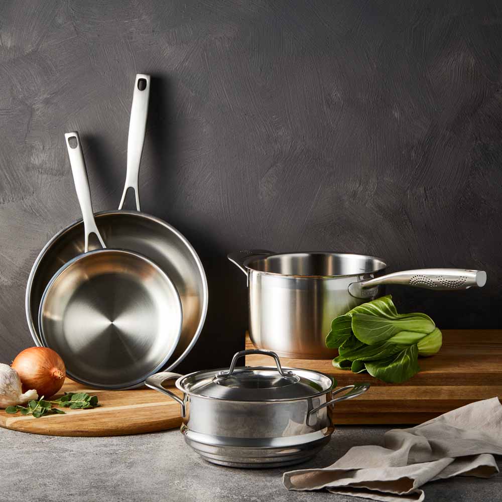 Four stainless steel cookware pieces on a gray surface including pots and pans with lid - Baccarat