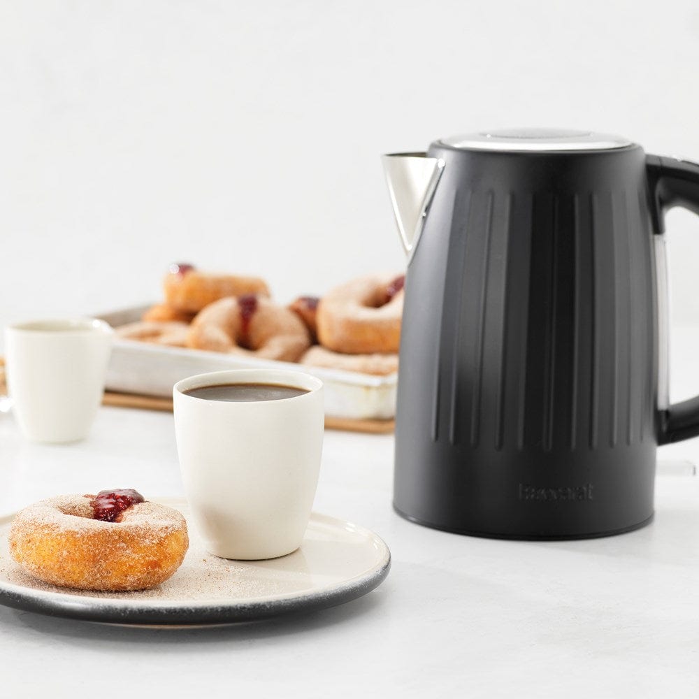 Black kettle pours hot water into a white cup beside a pastry plate - Baccarat Boiling Point Kettle