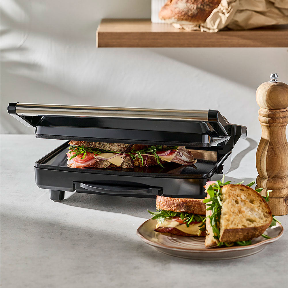 A lifestyle view depicts sandwiches being prepared next to the operating press.