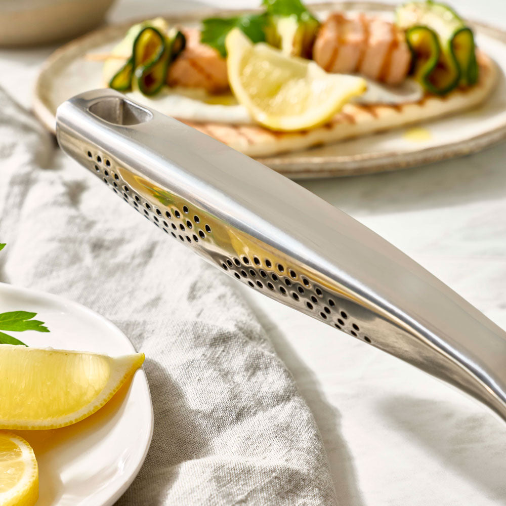 A close-up view focuses on the metal handle of a grill pan next to a plate of food and lemon slices.
