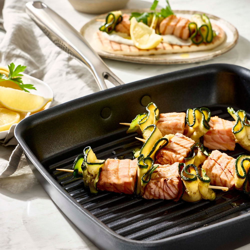 Skewers with meat and vegetables are resting inside a black ribbed grill pan.