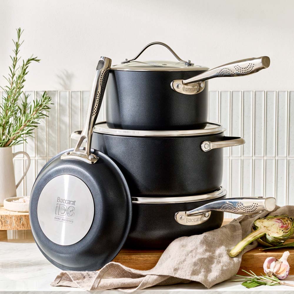 A stack of black pots and a frying pan is arranged on a kitchen counter in a lifestyle setting.