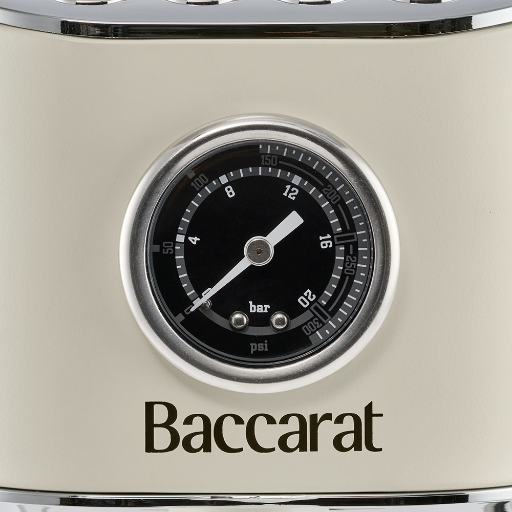A close-up view focuses on the pressure gauge and Baccarat logo on the front panel of a cream espresso machine.