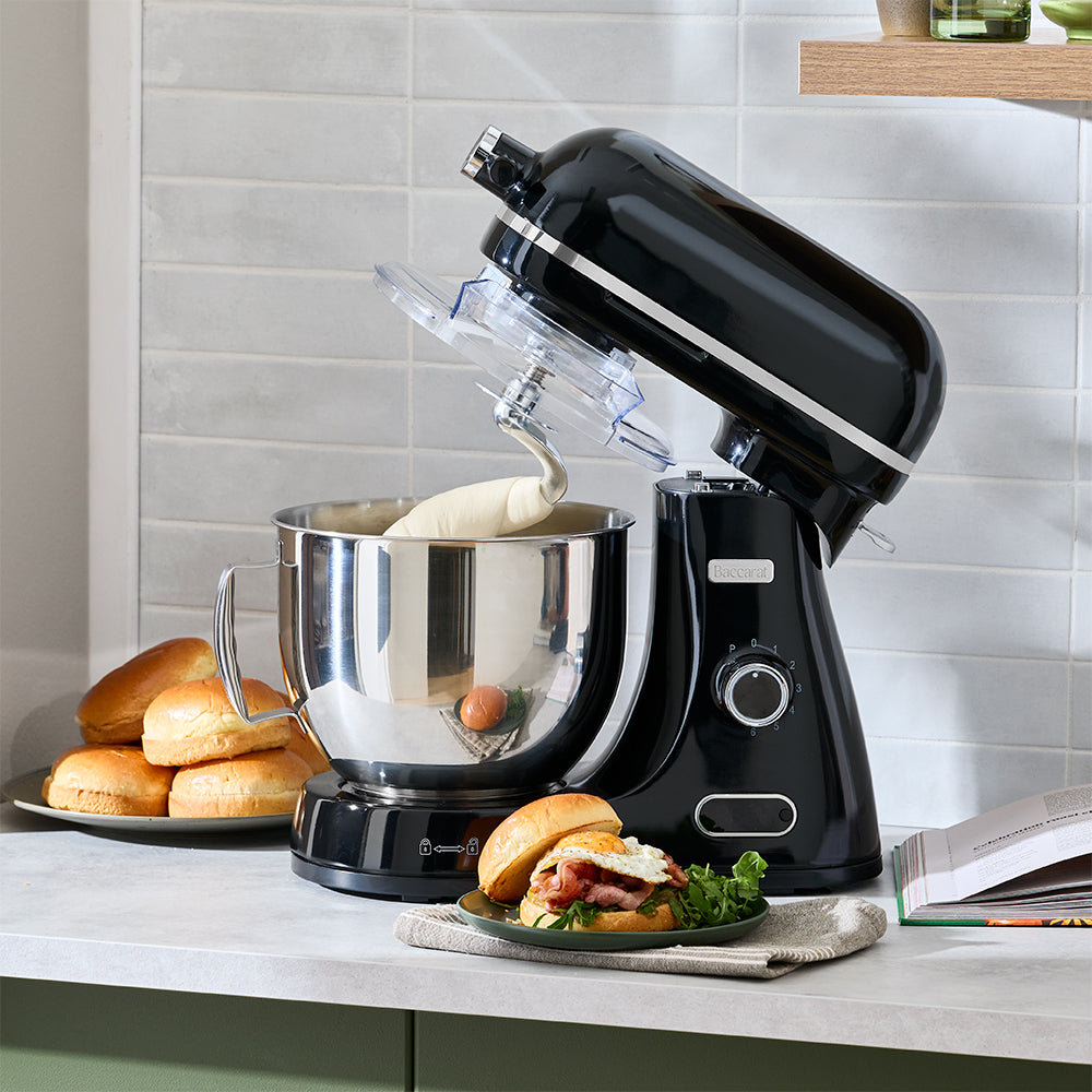 Black stand mixer with a bowl on a kitchen counter, surrounded by food items.