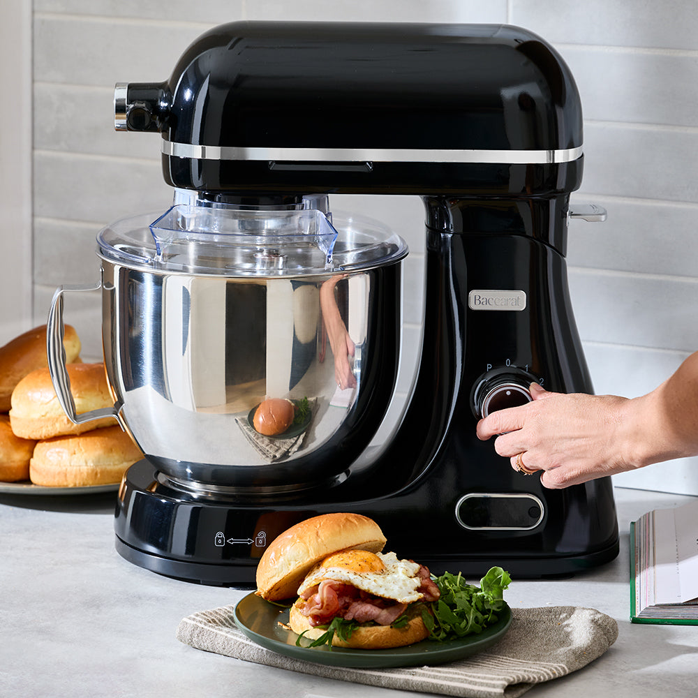 Black stand mixer on a kitchen counter with a sandwich and bread in the background