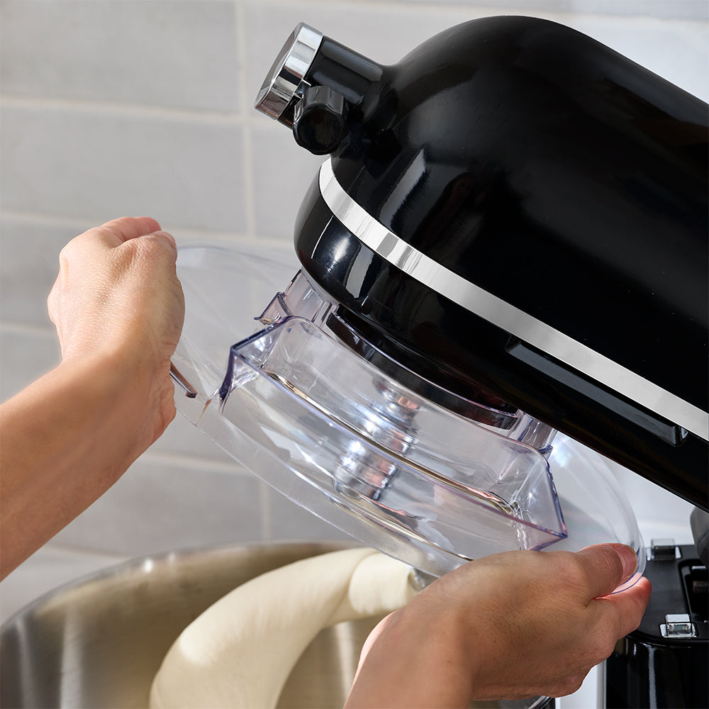 Person using a kitchen mixer with a clear attachment in a kitchen setting.