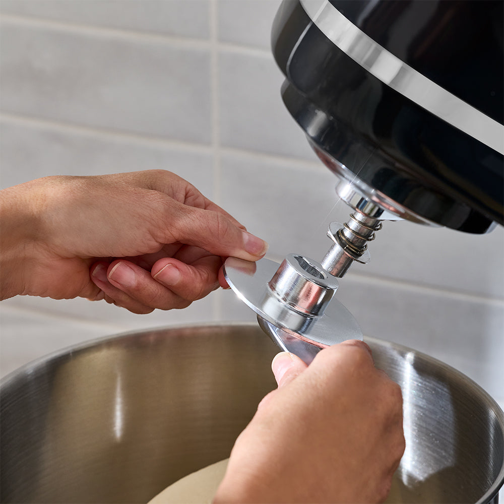 Person using a stand mixer with a bowl attachment on a tiled wall background