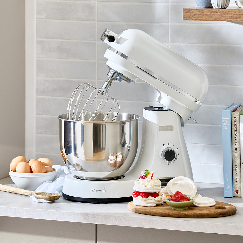 White stand mixer on a kitchen counter with baking ingredients and utensils.