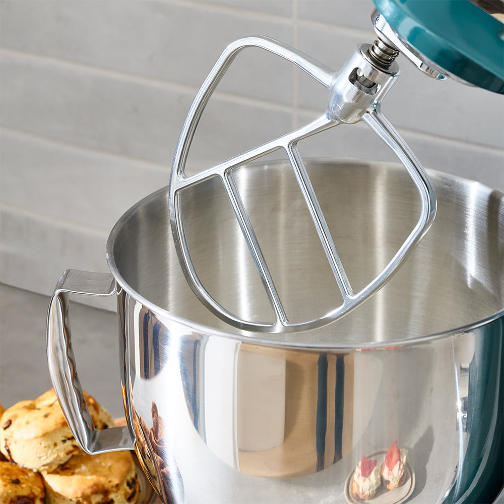 Metal stand mixer with a mixing bowl and paddle attachment on a kitchen counter.