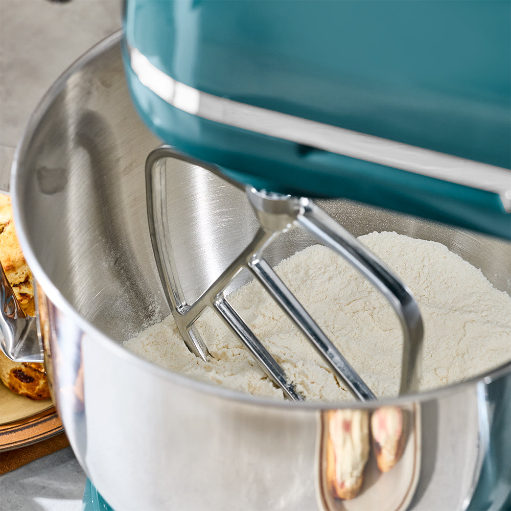 Teal stand mixer with metal bowl containing flour