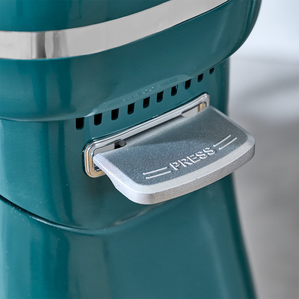 Teal coffee grinder with a 'PRESS' lever on a blurred background