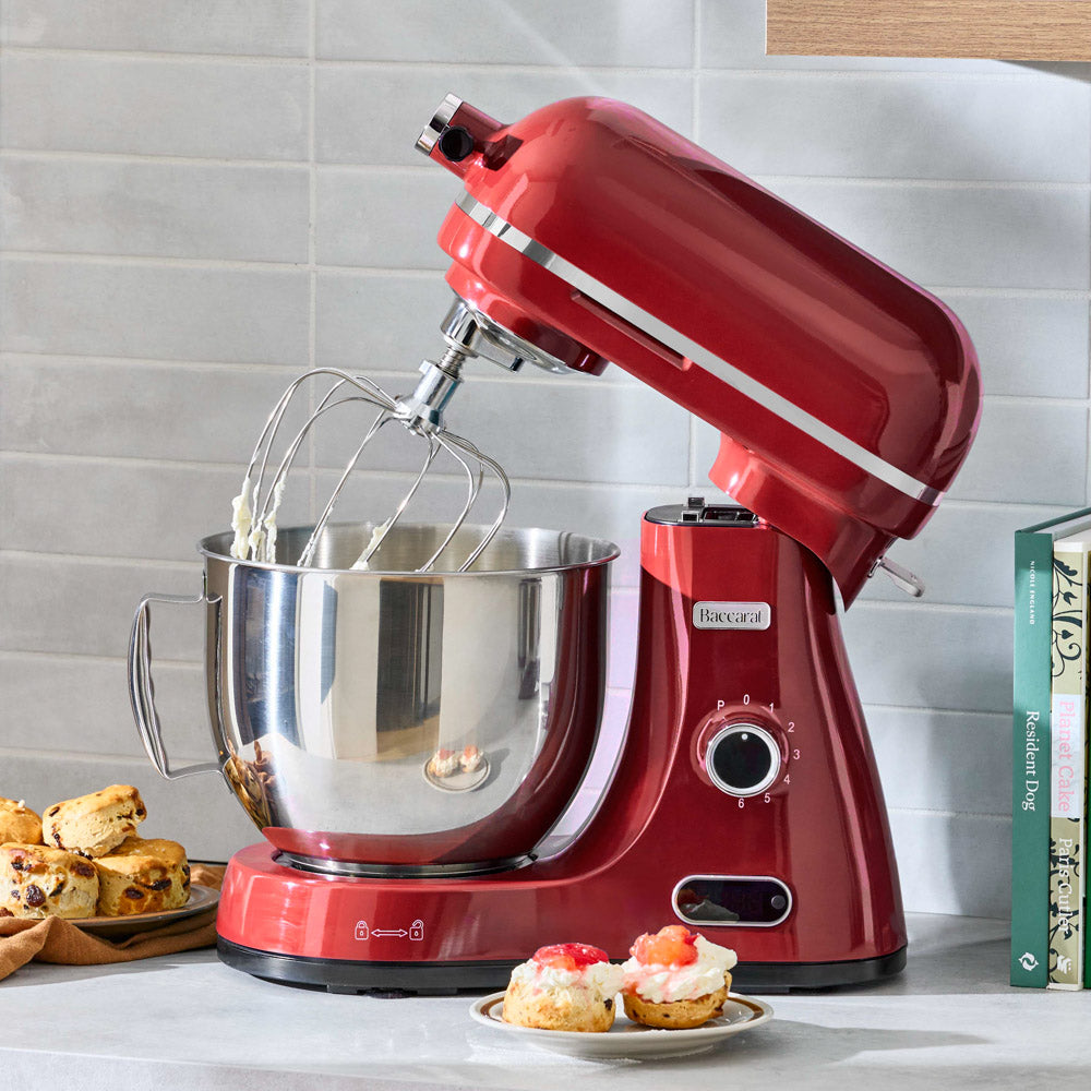 Red stand mixer with a bowl on a kitchen counter, surrounded by baked goods.