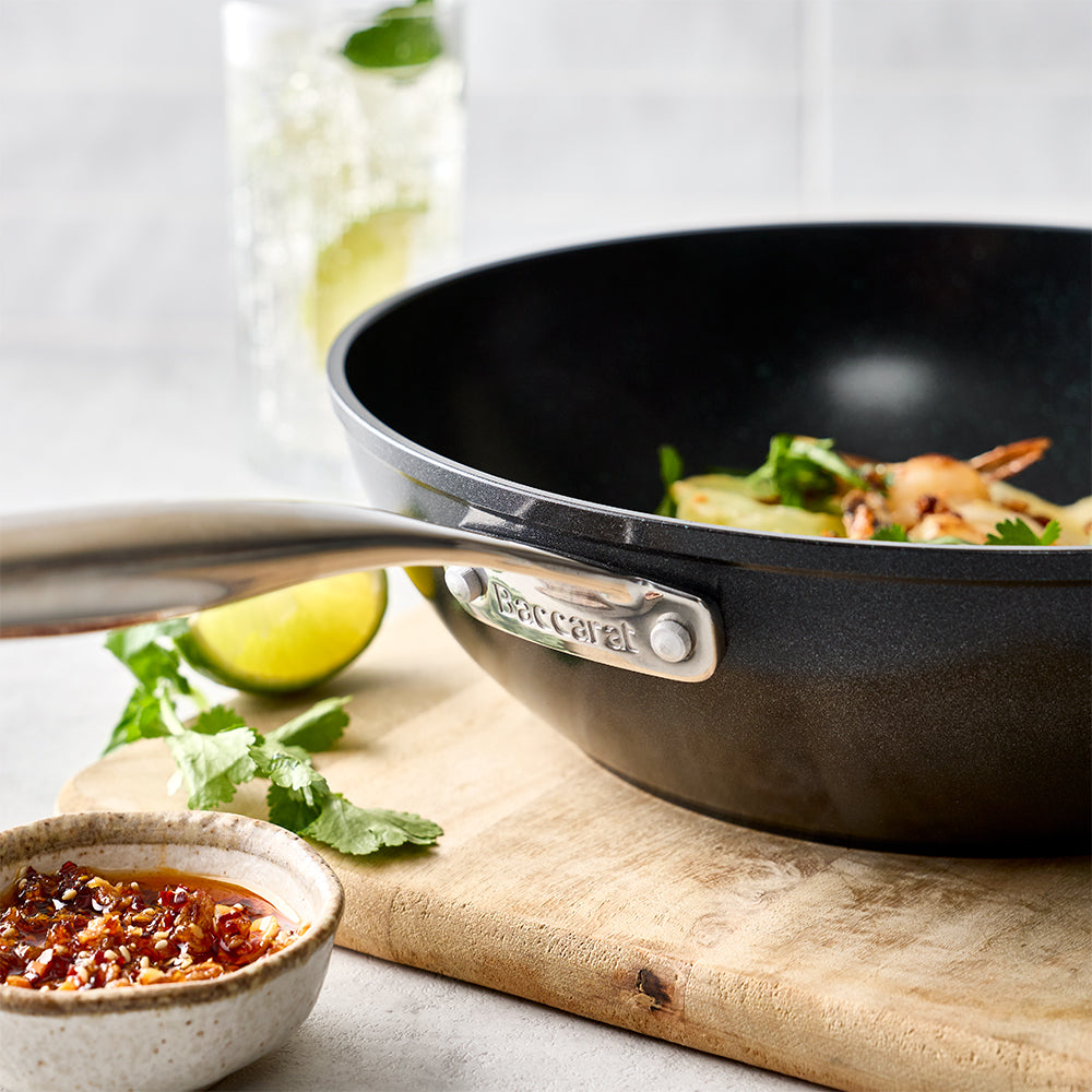 A close-up view focuses on the side of the black frying pan resting on a wooden board next to bowls of food and limes.