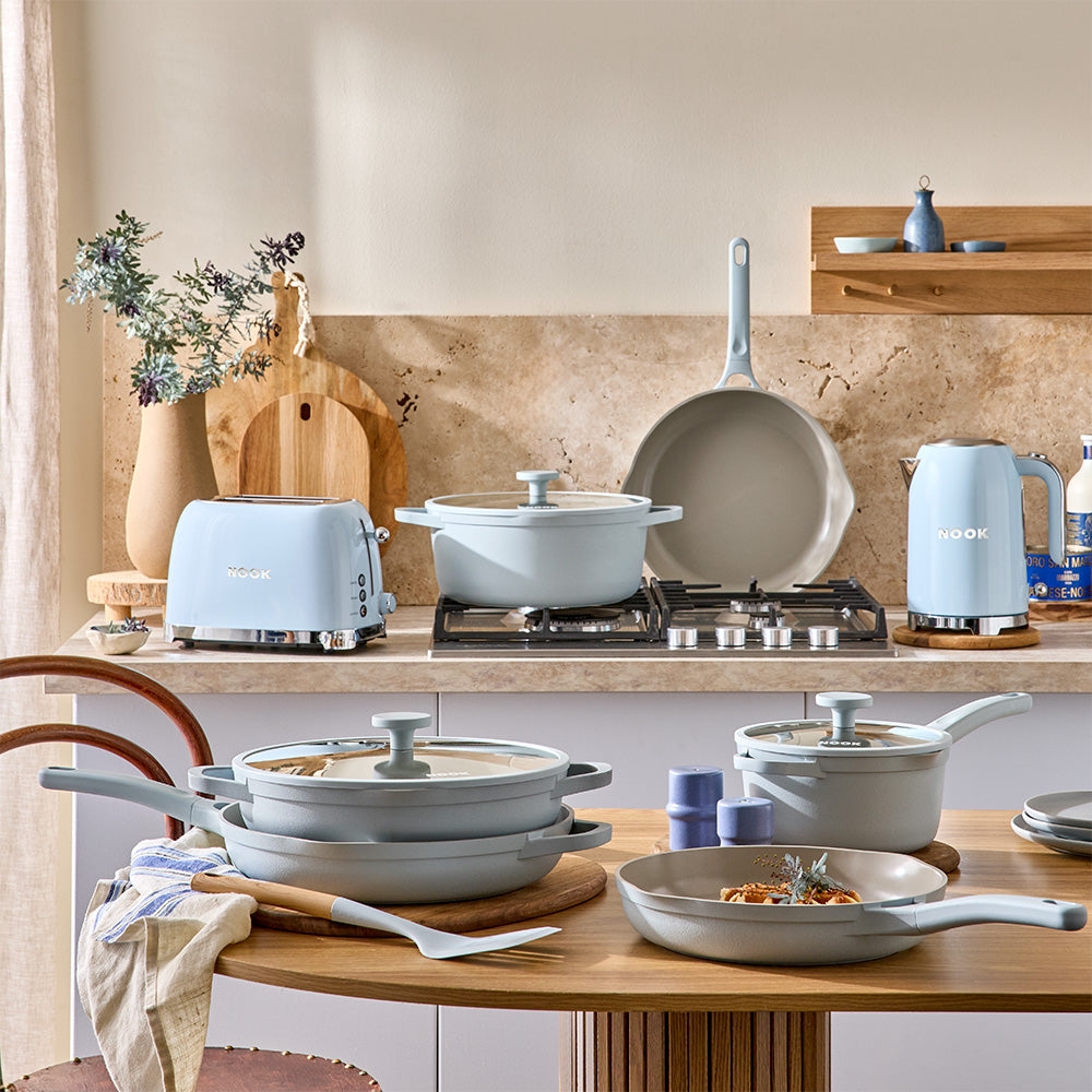 A coordinated kitchenware set in a warm, styled kitchen setting. The Sky collection is arranged on a wooden table and countertop.