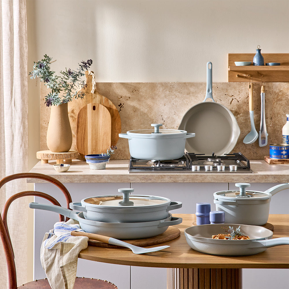 A wide kitchen shot shows light blue cookware sets, utensils, and matching small appliances arranged on the table and countertop.