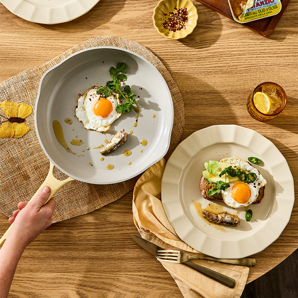 A person is holding the handle of a pastel yellow skillet filled with cooked food, topped with green chili 