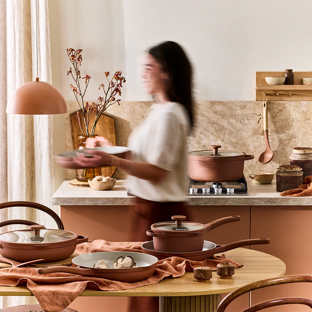 A woman is carrying a plate in a kitchen decorated with terracotta-colored cookware and matching utensils.