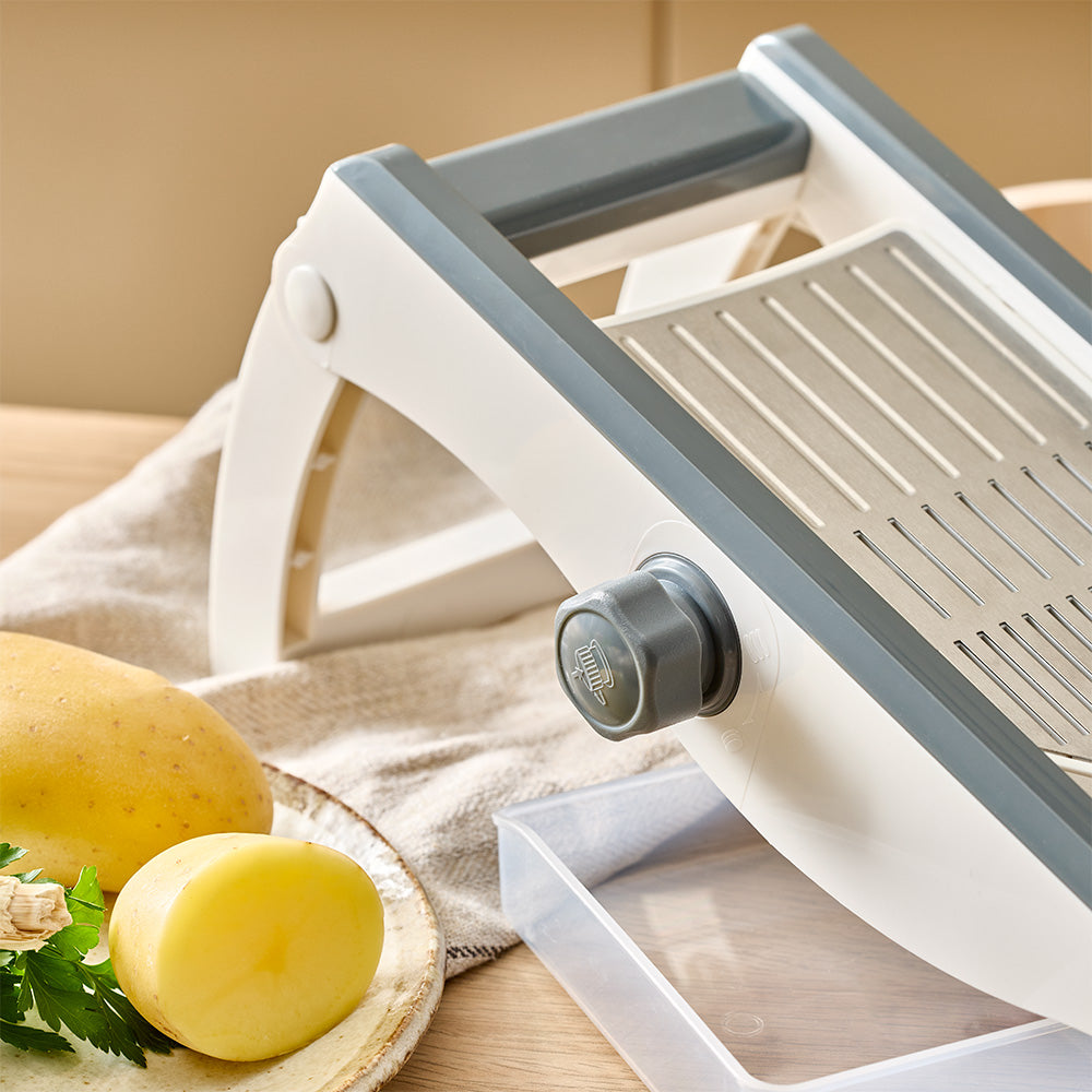 The side-mounted adjustment knob is visible next to a clear container and sliced potatoes on a wooden tabletop.