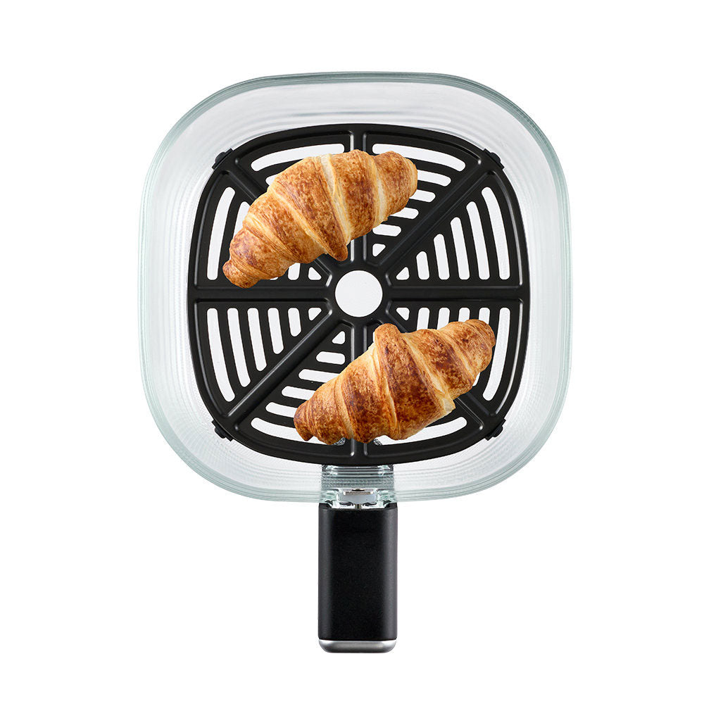 A countertop air fryer shown from the front on a white background, featuring a clear square outer shell, a black perforated basket, and two golden-brown croissants placed inside.