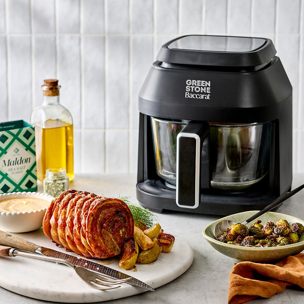 Black air fryer on a kitchen counter with roast chicken and side dishes in the background