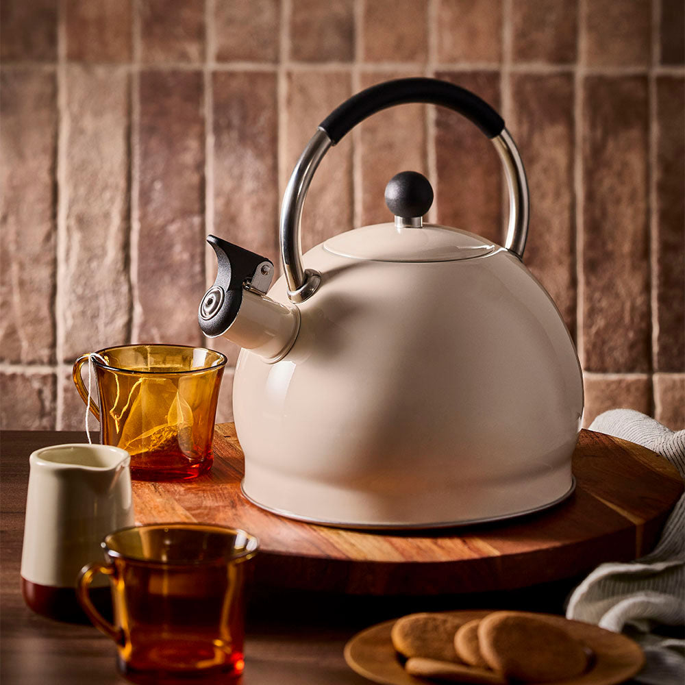 Oat stovetop kettle on a wooden board alongside an empty teacup containing a tea bag.