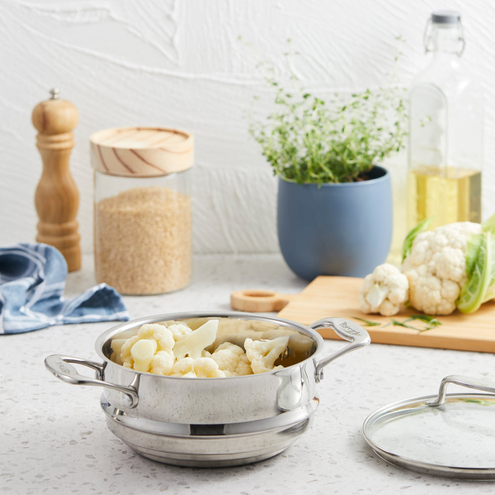 A set of polished stainless steel cookware with fresh vegetables on a wooden board - Baccarat Iconix