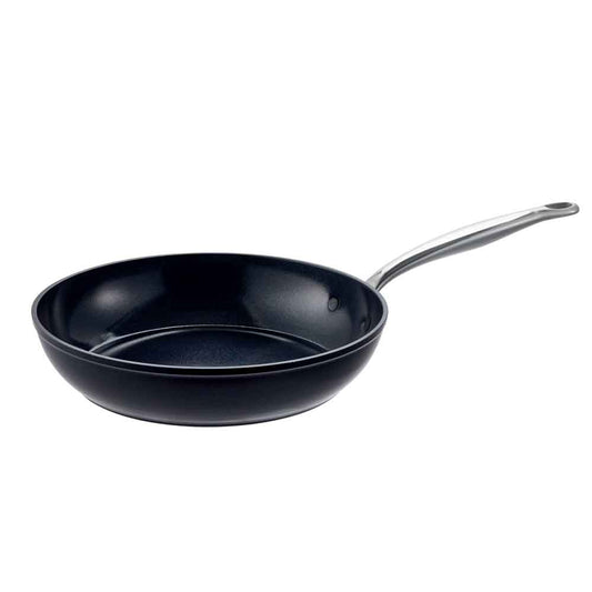 A Baccarat Le Connoisseurfrypan with pasta on a wooden board surrounded by olive oil and herbs