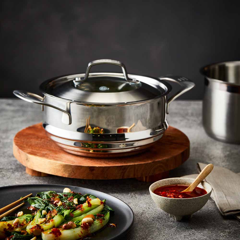 Four stainless steel cookware pieces on a gray surface including pots and pans with lid - Baccarat