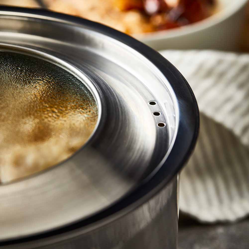 Four stainless steel cookware pieces on a gray surface including pots and pans with lid - Baccarat