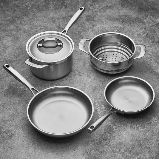 Four stainless steel cookware pieces on a gray surface including pots and pans with lid - Baccarat