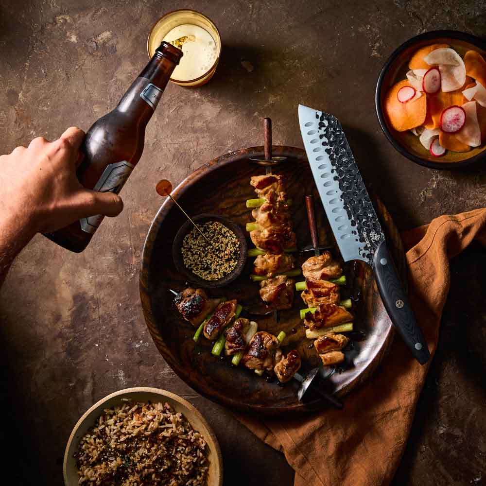 Man pouring beer beside Baccarat KUROI KIBA Santoku Knife 18cm at Baccarat
