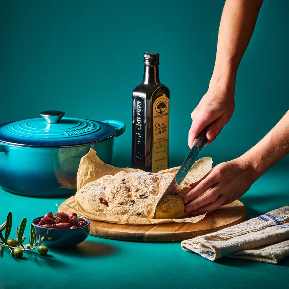 woman cutting bread baked from blue french oven - Baccarat