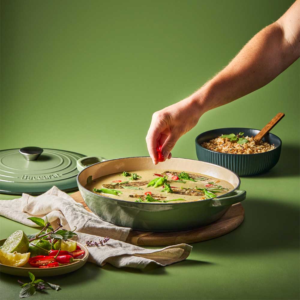 man sprinkling chilli into curry in green saute pan - Baccarat
