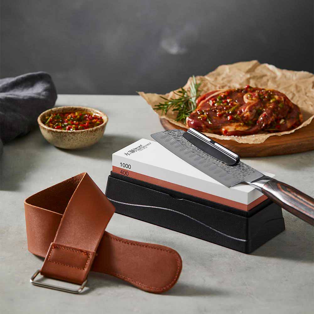 santoku knife sitting on a whetstone with leather strop - Baccarat