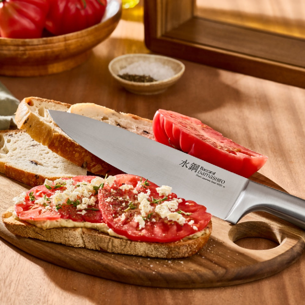 Knife on a wooden cutting board with a slice of bread topped with tomato and cheese