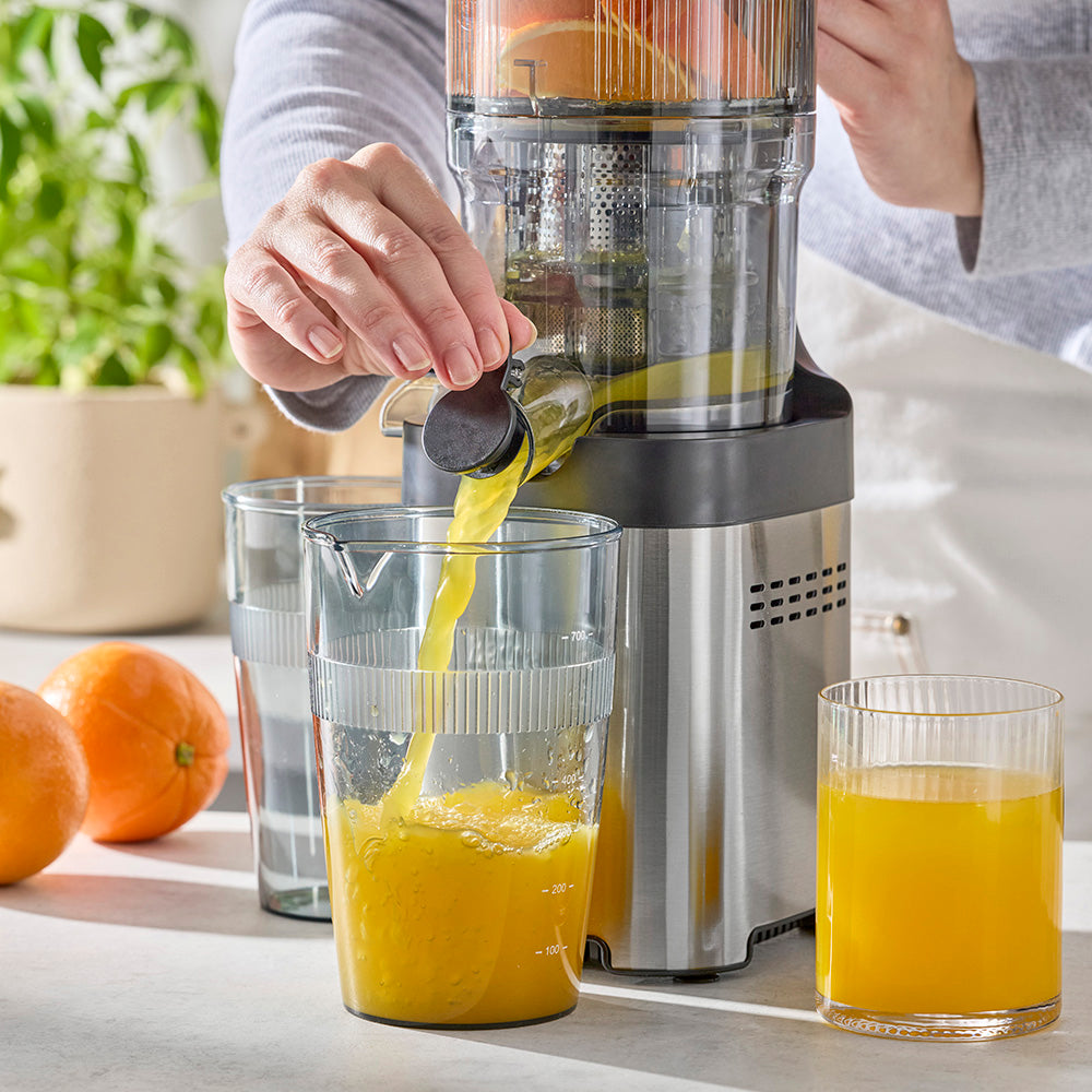 Person using a manual juicer to extract orange juice into glasses.